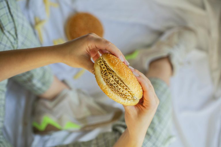 A creative concept showing a close-up of hands holding a burger with jewelry inside.